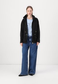 Μαύρο φούτερ μπουφάν με χρυσές λεπτομέρειες, συνδυασμένο με ένα ανοιχτό μπλε πουκάμισο με λουλούδια και πλατύ παντελόνι μπλε τζιν. Μαύρες μυτερές γόβες ολοκληρώνουν την εμφάνιση.