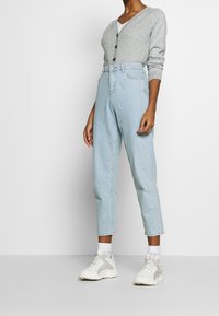 Jeans a vita alta di colore blu chiaro con gamba dritta, dotati di tasche anteriori e chiusura con bottone, abbinati a un cardigan grigio con bottoni.