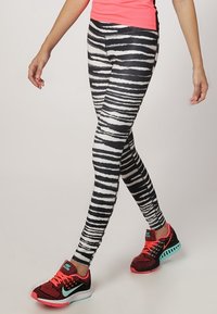 Leggings à rayures noires et blanches avec une coupe extensible, associées à des chaussures de sport rouge et noir avec un accent turquoise.