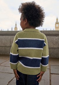 Kootud kampsun roheliste, mereväe ja valgete triipudega, kraega ja tekstuurse kangaga, kantud tumedate teksapükste kohal.