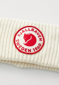 Roomkleurige geribbelde tricotstof met een ronde rood-witte patch met een voskop en de tekst "Fjällräven Sweden 1960."
