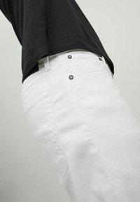 Vaqueros de denim blancos con un corte ajustado, diseño de cinco bolsillos y herrajes metálicos. La textura es suave y la tela parece ligeramente elástica.