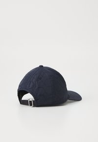 Boné de beisebol matelassado em azul-marinho, com padrão hexagonal, faixa traseira ajustável e aba curva. Retratado a partir de um ângulo traseiro.