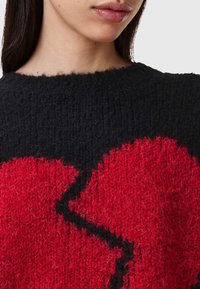 Sweter dzianinowy w czarno-czerwono-czarny zygzakowaty wzór. Teksturowany materiał z okrągłym dekoltem i luźnym krojem.