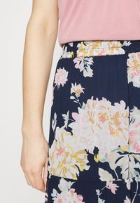 Falda floral en azul marino con flores rosas y amarillas, con una cinturilla fruncida y textura fluida. Camiseta en suave rosa está encima.