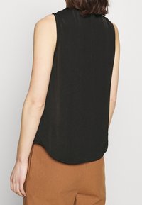 Haut noir sans manches avec un ourlet incurvé, fabriqué en tissu lisse. Le dos présente un décolleté discret et aucun détail supplémentaire.