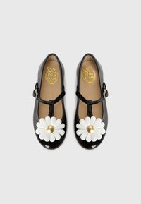 Schwarze Lack-Mary-Jane-Schuhe mit weißen Gänseblümchen-Dekorationen und goldenen Mitteln, beige Innensohlen mit goldfarbenem "POM D'API"-Logo.