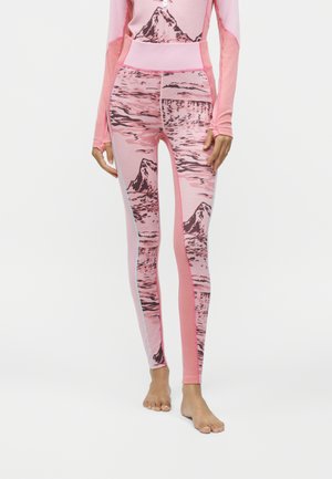 Femme portant un legging rose avec imprimé montagne et paysage, debout pieds nus sur un fond blanc uni.