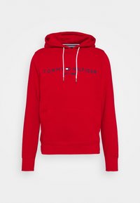 Sweat-shirt à capuche rouge avec cordons blancs, poche kangourou à l'avant et texte "Tommy Hilfiger Est. 1985" avec logo sur la poitrine.