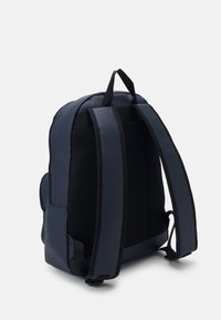 Zaino blu navy con spallacci imbottiti e pannello posteriore testurizzato. Caratterizzato da una forma snella e due tasche laterali per la conservazione.