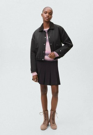 Veste noire courte avec un col sombre, pull en tricot rose, jupe noire plissée et bottes lacées beiges. Design minimaliste et tissus texturés.