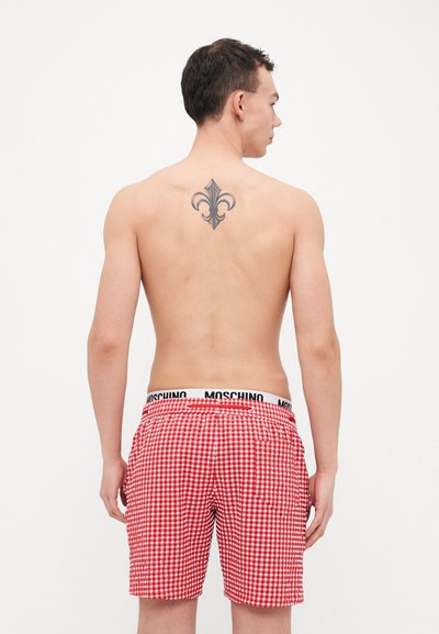Raudoni langeliai maudymosi šortai su elastine Moschino juosta, detalė kišenėje gale ir tatuiruotė su fleur-de-lis modeliui ant nugaros.