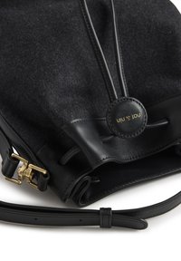 Crna filc torba s crnim kožnim detaljima, zlatnim metalik ukrasima i kružnim logotipom. Ima zatvaranje na vezicu i podesivu naramenicu.