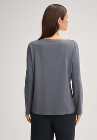 Šedý dlouhý rukáv top s kulatým výstřihem, vyrobený z měkkého, hladkého materiálu, s rovnými liniemi a volným střihem, doplněný tmavými kalhotami.