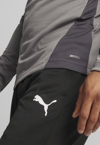 Grijze sportshirt met een gestructureerd zijpaneel en het "DRYCELL"-logo, gecombineerd met zwarte broek met een wit Puma-logo.