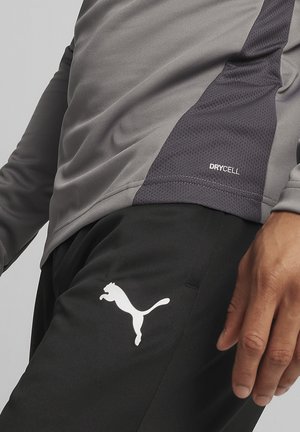 Das graue Sportshirt verfügt über ein strukturiertes Seitenpaneel und das "DRYCELL"-Logo, kombiniert mit schwarzen Hosen, die ein weißes Puma-Logo zeigen.