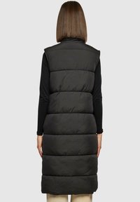 Gilet noir rembourré au design sans manches, présentant des panneaux matelassés horizontaux, un col haut et une longueur allant jusqu'au mi-mollet.