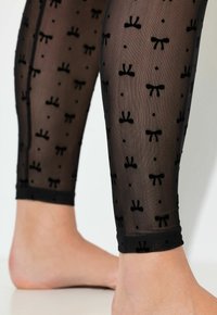 Černé průsvitné legíny s malým černým mašličkovým a puntíkovým vzorem. Mají jemnou texturu, elastický pas a končí těsně nad kotníkem.