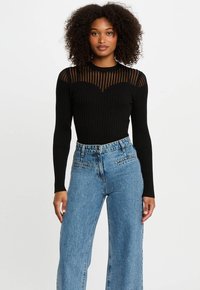 Top nero a maniche lunghe con righe orizzontali trasparenti sulle spalle, abbinato a jeans a vita alta in denim blu chiaro con gamba larga.