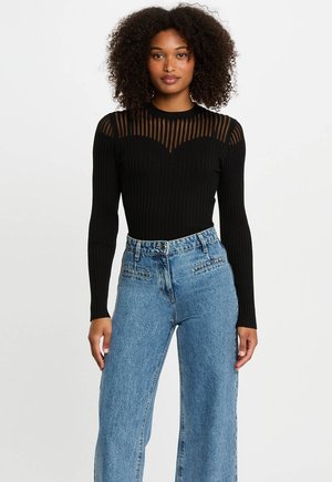Black ribbed long-sleeve top with sheer horizontal stripes across the shoulders, paired with high-waisted light blue wide-leg jeans.