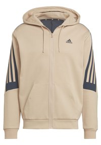 Sweat à capuche zippé beige avec capuche doublée, poches avant et accents bleu marine. Présente trois bandes bleues marines sur chaque manche et un logo Adidas.
