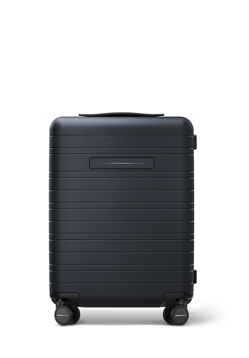 Valise rigide bleu foncé avec des rayures horizontales texturées, poignée robuste et quatre roues noires pour une manœuvrabilité facile.