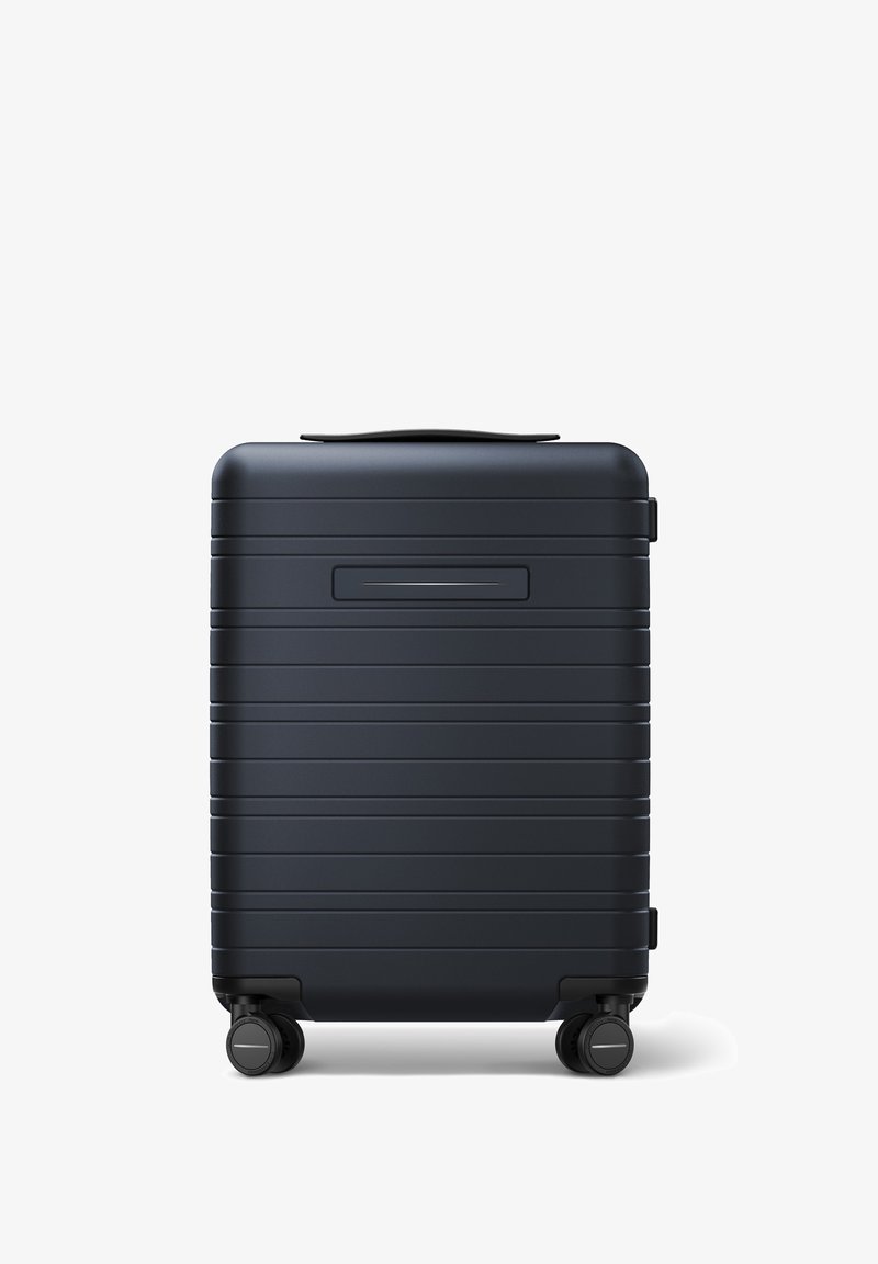 Valise rigide bleu foncé avec des rayures horizontales texturées, poignée robuste et quatre roues noires pour une manœuvrabilité facile.