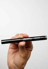 Zwarte, langdurige oogschaduwstick met een afgeronde punt, met witte tekst en een groene accent aan de bovenkant, vastgehouden in een hand.