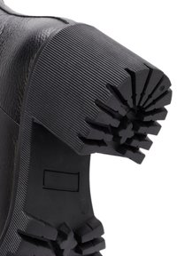 Zwarte leren schoen met een gestructureerde, patroonrubberen zool met uitgesproken profiel en een lichthellende hak.