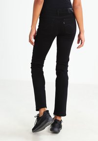 Svart denimjeans med smal passform, med bakfickor som visar ett klassiskt sömnadsdiagram. Bärs med svarta sportskor.