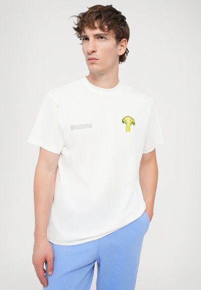 T-shirt en coton blanc avec un graphique de brocoli vert sur la poitrine gauche et du texte sur le côté. Encolure ras du cou et manches courtes.