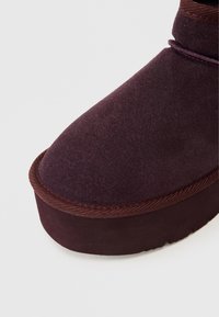 Ankelhöga, plommonfärgade stövlar i mjukt mocka med rund tå, utrustade med en texturerad gummisula och kontrasterande brun kant.