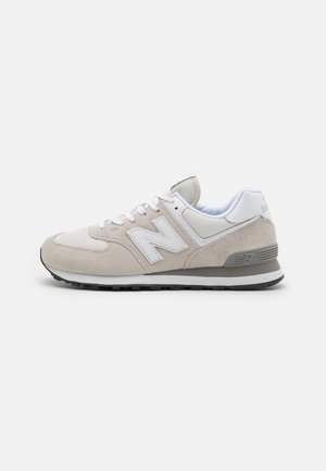 Baskets New Balance beige et blanches avec panneaux en suède et mesh, lacets blancs et semelle en caoutchouc noire, vues de profil.