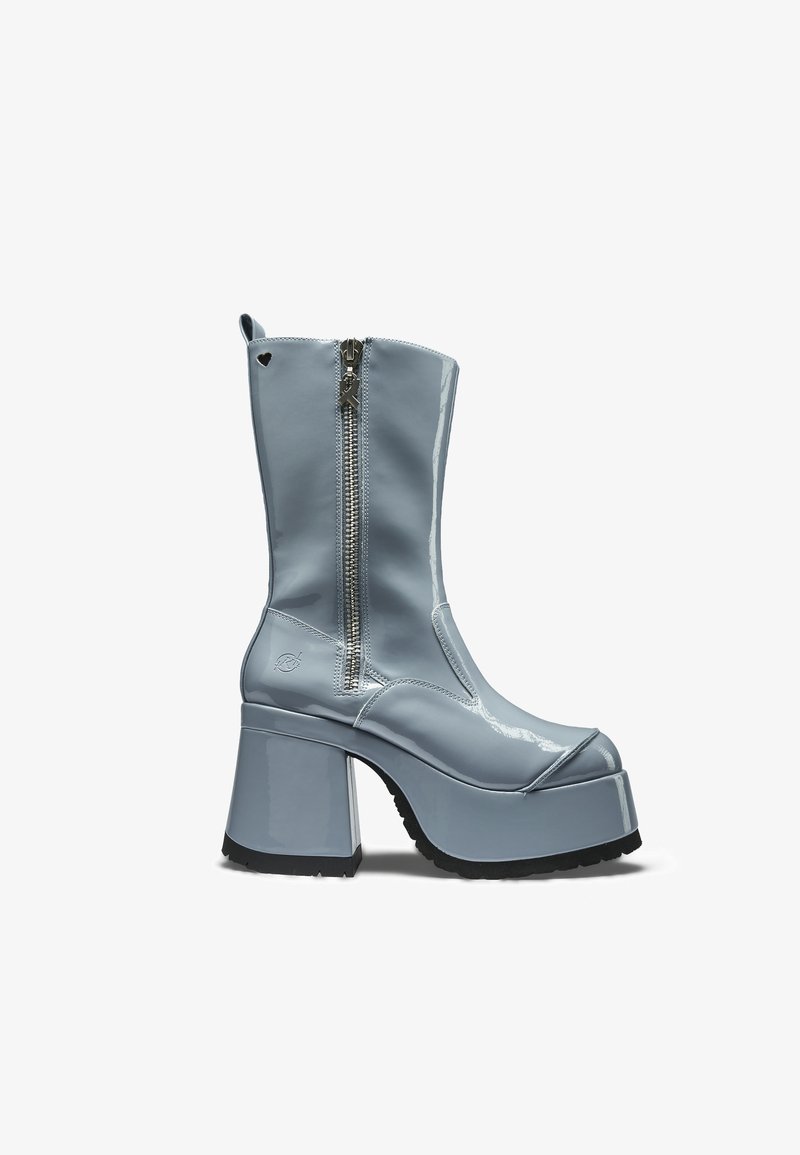 Mėlynos lakinės odos platforminio stiliaus batai su masyviu kulnu, šoniniu užtrauktuku ir nedideliu širdelės formos išpjovimu šalia viršaus.