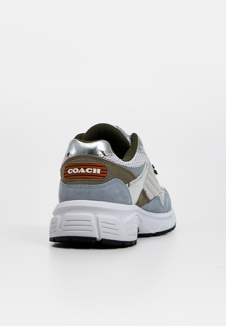 De sneaker heeft een grijs, wit en groen kleurenschema met zilveren accenten. Het ontwerp bevat een dikke zool en een gemarkeerde tab aan de hak.