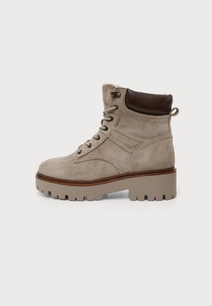 Bottine beige en daim avec col matelassé marron foncé, laçage à l'avant et semelle en caoutchouc épaisse à crampons.