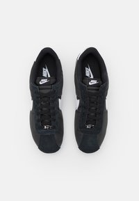 Svarta Nike-sneakers i en kombination av läder och mocka, med vita logotypdetaljer och platta svarta snören. Klassisk design.