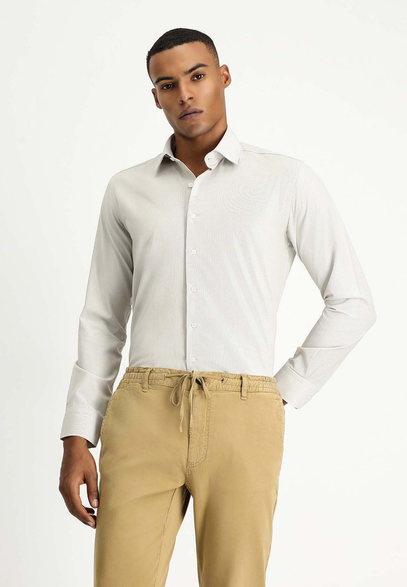 Hellgraues Langarmhemd mit Knopfleiste, subtiler Textur und spitzem Kragen, kombiniert mit beigen Jogginghosen mit Kordelzug.