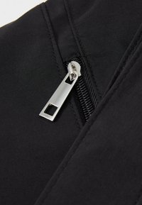 Tecido preto com uma abertura com fecho, apresentando uma aba retangular em prata, exibindo uma textura suave e detalhes de costura em close-up.