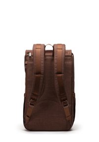 Brun tygryggsäck med två justerbara remmar, ett handtag upptill, sidofickor och en elegant rektangulär form. Dragkedjeslutning.