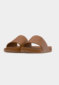 Sandalias marrones sin cordones con correas estampadas y logotipos en relieve en el lateral, con suela plana y diseño de punta abierta.