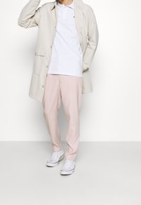 Hellbeige Jacke, weißes Polohemd und sanft rosa Hose, ergänzt mit weißen Sneakers; lässiges und modernes Design.