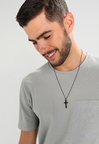 Lys grå kortermet T-skjorte med brystlomme, sammen med et svart korsanheng. Myk tekstur, uformelt design.