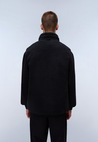 Black fleece vest with a high collar, textured fabric, sleeveless design, and a relaxed fit. Back view shows smooth, seamless edges.