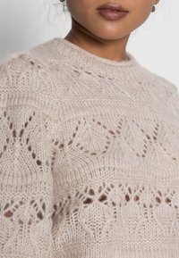 Suéter de punto rosa claro con delicados patrones de encaje y puntadas texturizadas. Presenta un cuello redondo y mangas largas, fabricado con material suave y esponjoso.