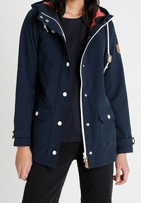 Navy waterproof jacket with a hood, white zipper, and snap buttons. Features side pockets and a contrasting inner lining. Smooth texture.