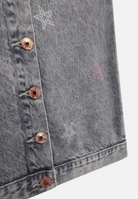 Denimkleidung aus grauem Stoff mit Silber- und rosa Sterne-Stickerei. Fünf bronzefarbene Knöpfe verzieren die Vorderseite und den Saum.