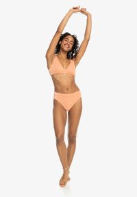 Őszibarack bikini szett, háromszög alakú top és magas derékú alsó résszel. Az anyaga simának tűnik, bordázott textúrával, minimalista dizájnnal.