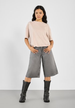 Vaaleanpunainen, ylisuuri lyhythihainen T-paita, yhdistettynä harmaisiin culottes-housuihin ja polvenkorkuisiin mustiin saappaisiin, joissa on metallisia yksityiskohtia.