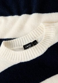 Sweter w paski w kolorach granatowym i kremowym z prążkowanym, okrągłym dekoltem. Wykonany z miękkiego, fakturowanego materiału. Metka na karku wskazuje markę LMTD.